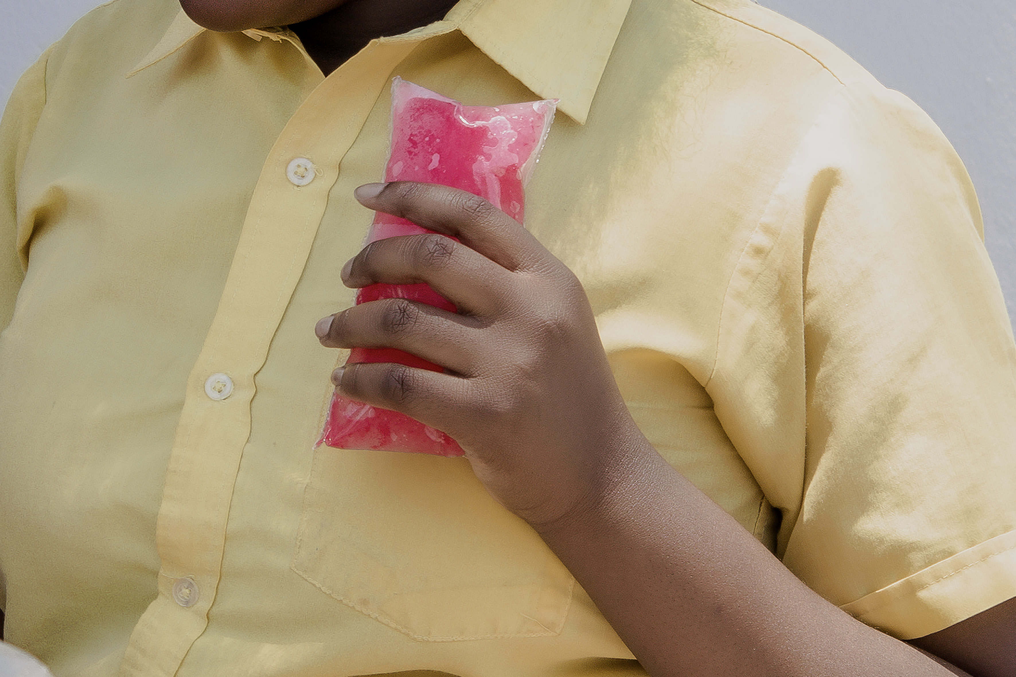 a girl in a yellow shirt holding a pink popsicle in front of her